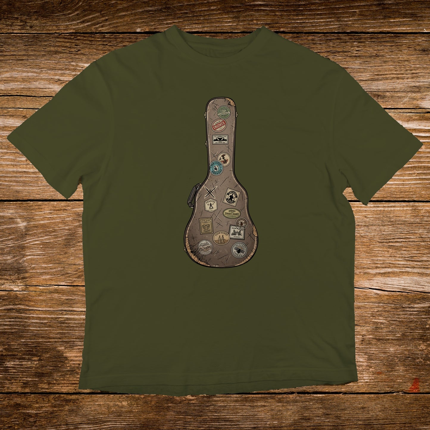 Olive t-shirt with a brown guitar case graphic adorned with travel stickers.
