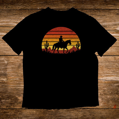 Silhouette of cowboy on horseback against a sunset and cacti.
