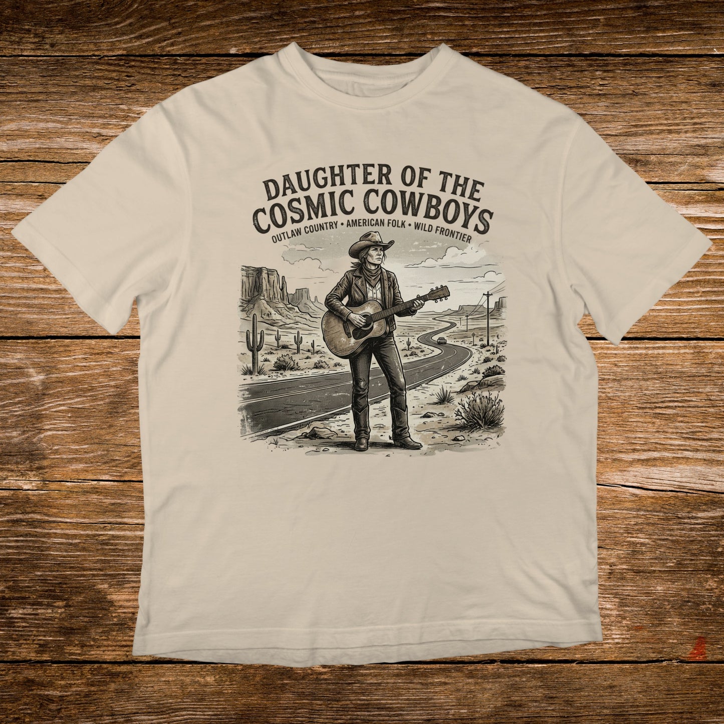 T-shirt graphic of a cowboy playing guitar on a desert road, "Daughter of the Cosmic Cowboys" text.