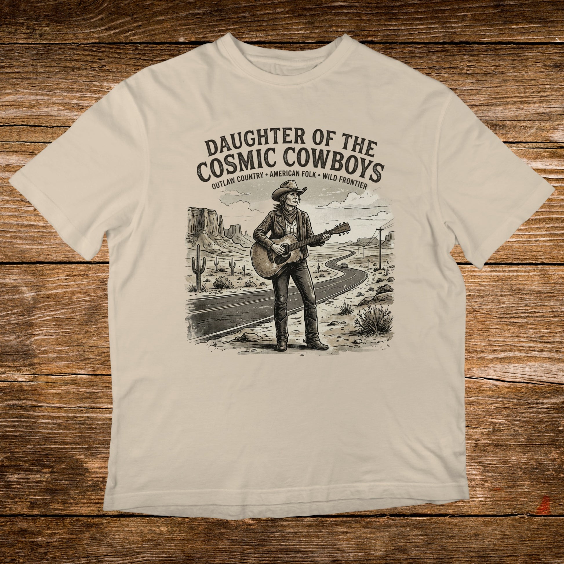 T-shirt graphic of a cowboy playing guitar on a desert road, "Daughter of the Cosmic Cowboys" text.