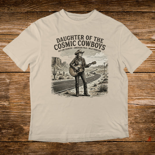 T-shirt graphic of a cowboy playing guitar on a desert road, "Daughter of the Cosmic Cowboys" text.