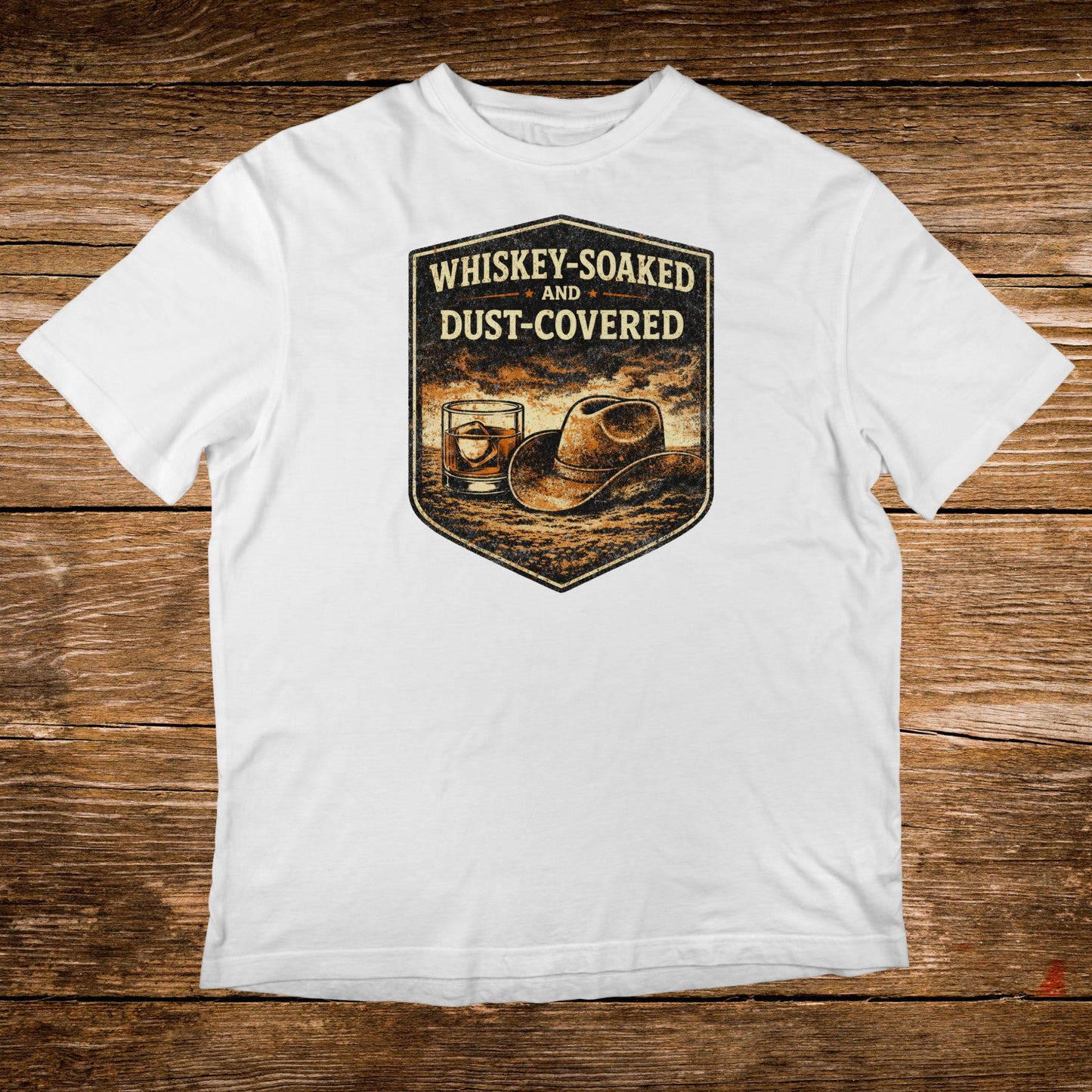 White t-shirt with "Whiskey-Soaked AND Dust-Covered" text and whiskey glass and hat illustration.