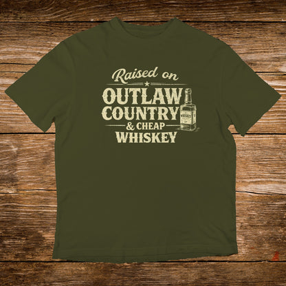 Olive green t-shirt with "Raised on Outlaw Country & Cheap Whiskey" text and whiskey bottle graphic.