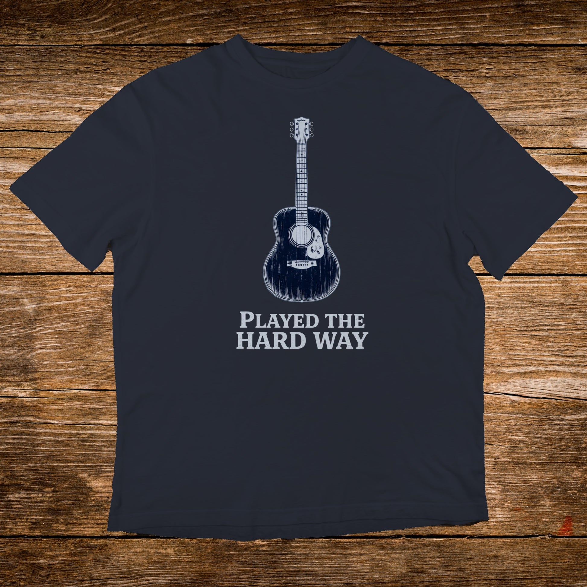 Dark t-shirt with a graphic of an acoustic guitar and text "PLAYED THE HARD WAY".