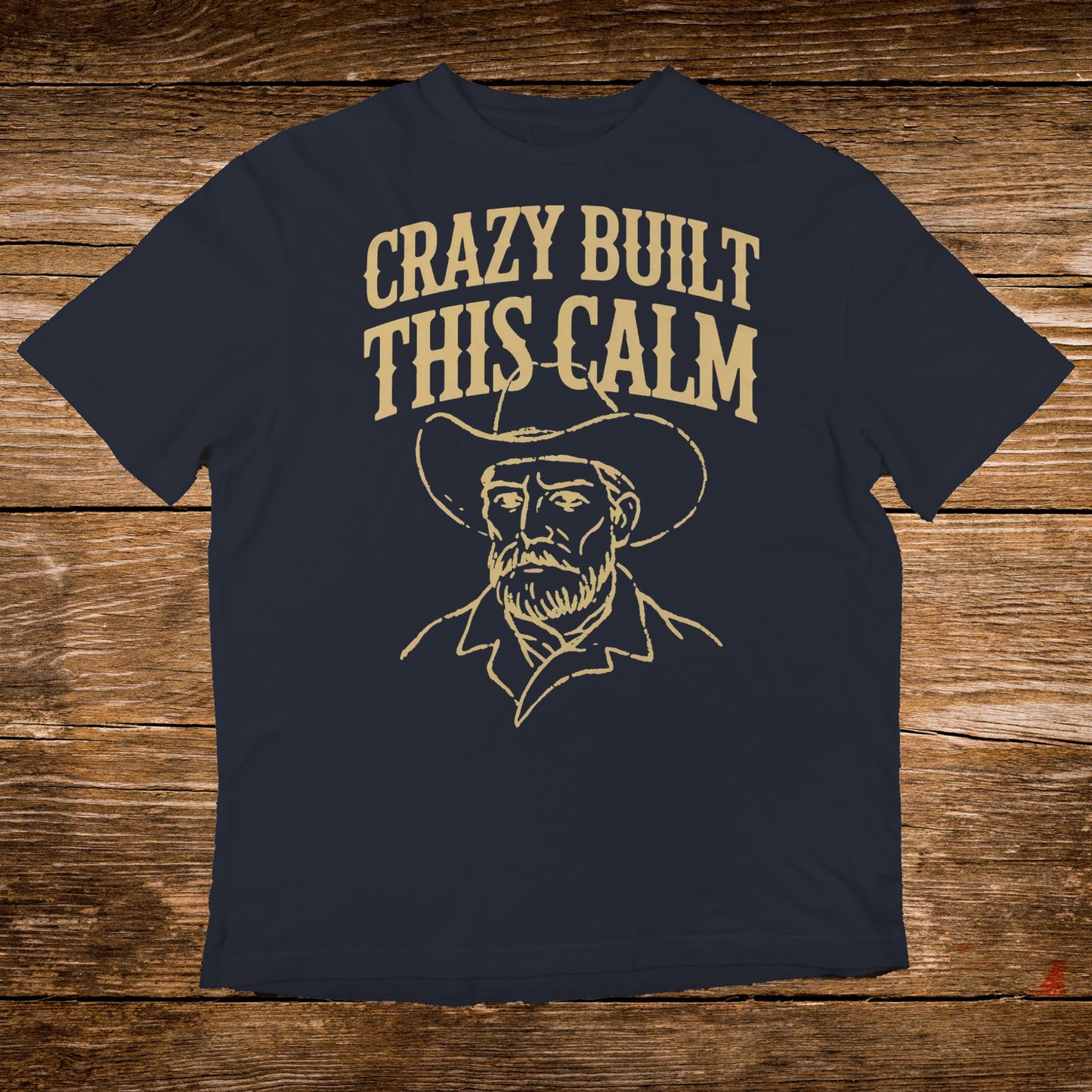 Dark t-shirt with a line drawing of a cowboy and "CRAZY BUILT THIS CALM" text.