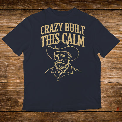 Dark t-shirt with a line drawing of a cowboy and "CRAZY BUILT THIS CALM" text.