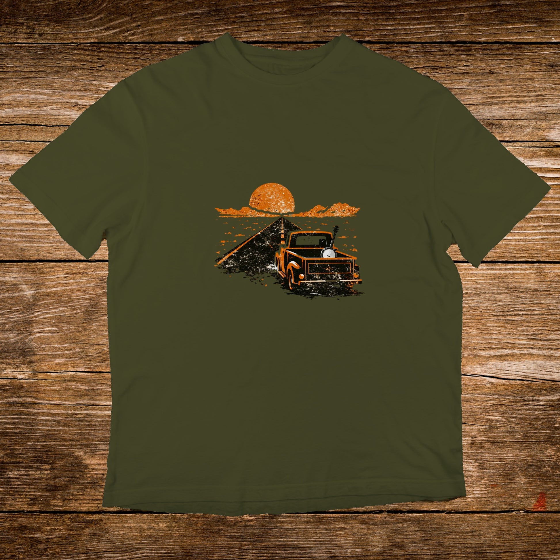Olive green t-shirt with a vintage truck and sunset graphic on a wooden background.