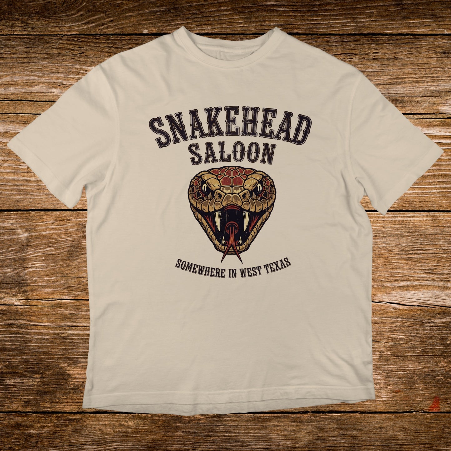 Cream t-shirt with Snakehead Saloon logo featuring a snake's head and "Somewhere in West Texas".