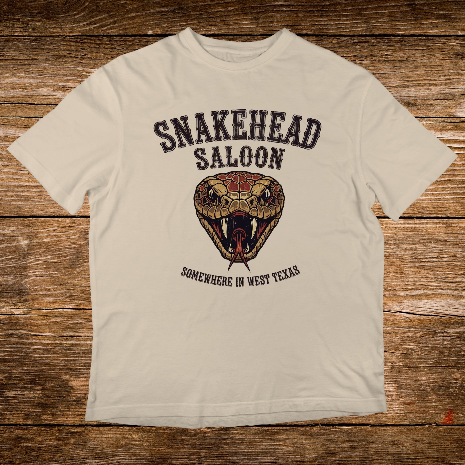 Cream t-shirt with Snakehead Saloon logo featuring a snake's head and "Somewhere in West Texas".