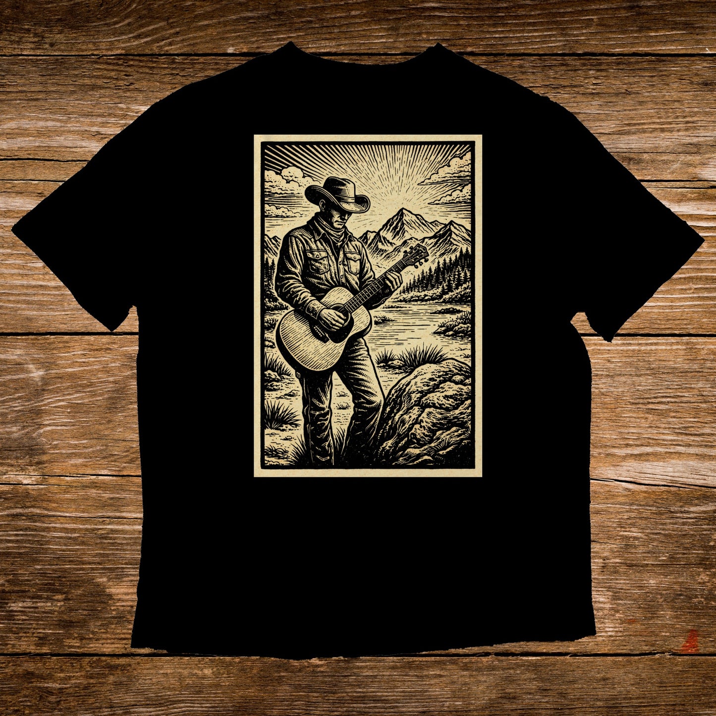 Black t-shirt featuring illustration of cowboy playing guitar in scenic mountain landscape.