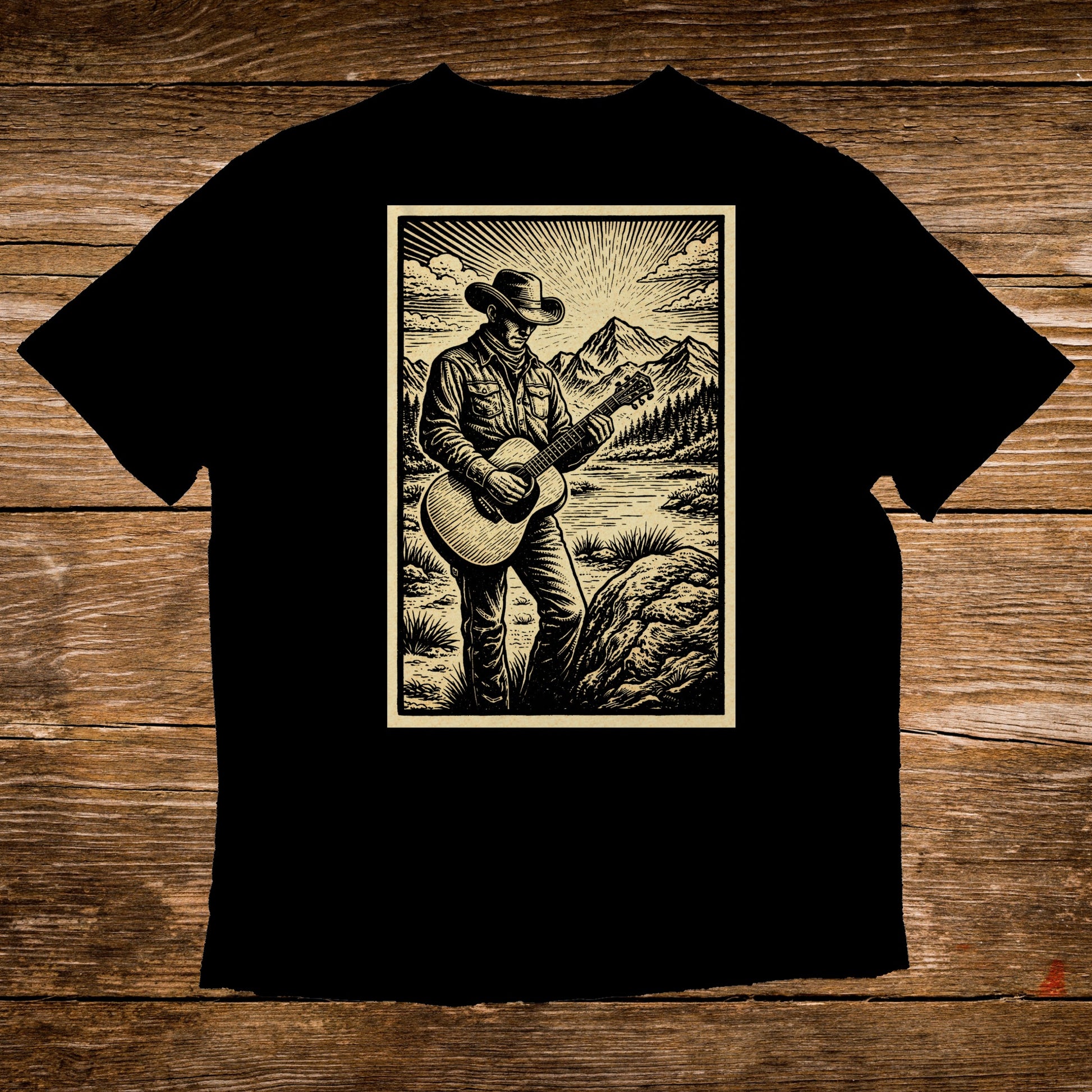 Black t-shirt featuring illustration of cowboy playing guitar in scenic mountain landscape.